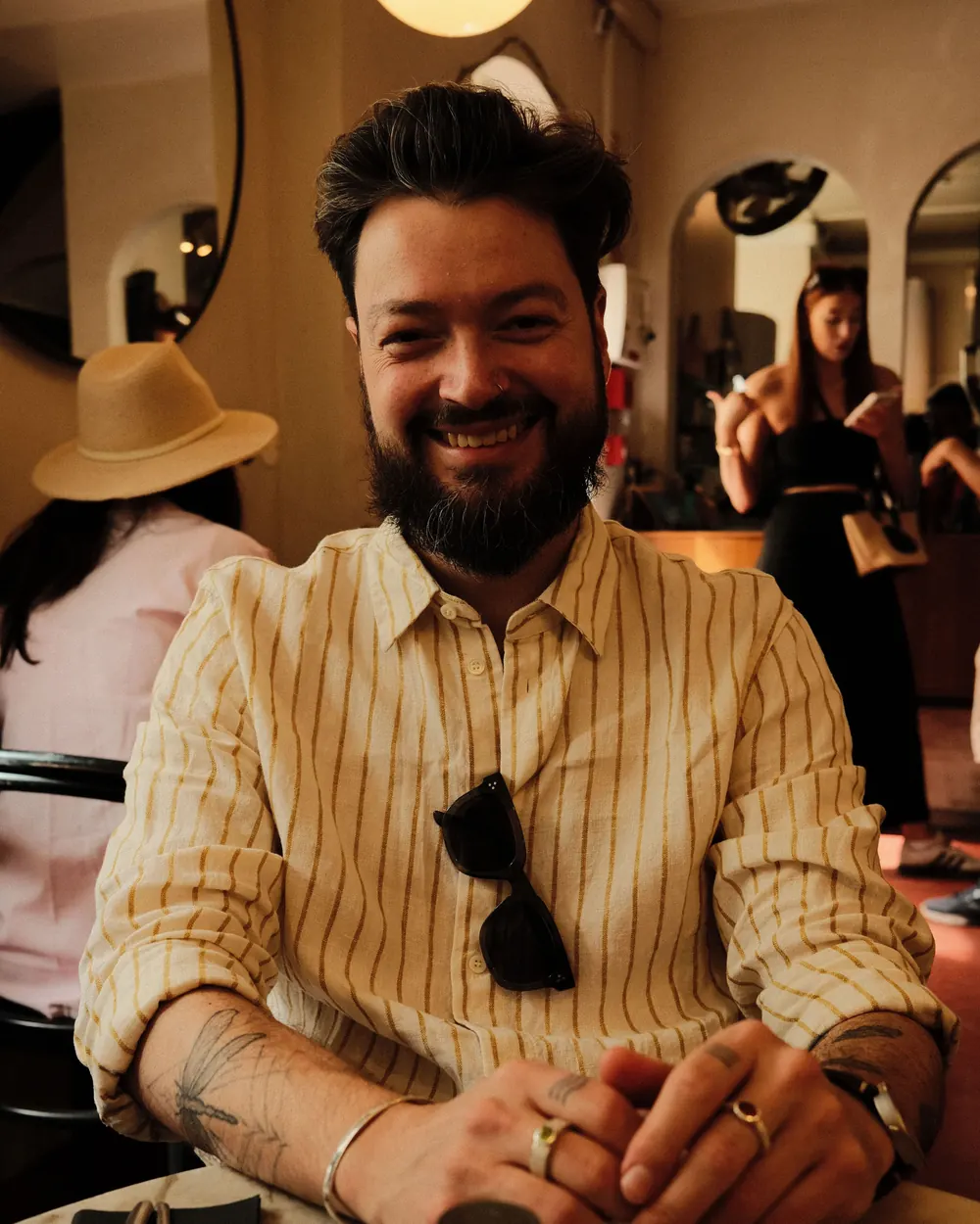 Portrait of Gerrit Weber: a smiling man with sunglasses and a beard, wearing a yellow striped shirt inside a boutique café in Lisbon.